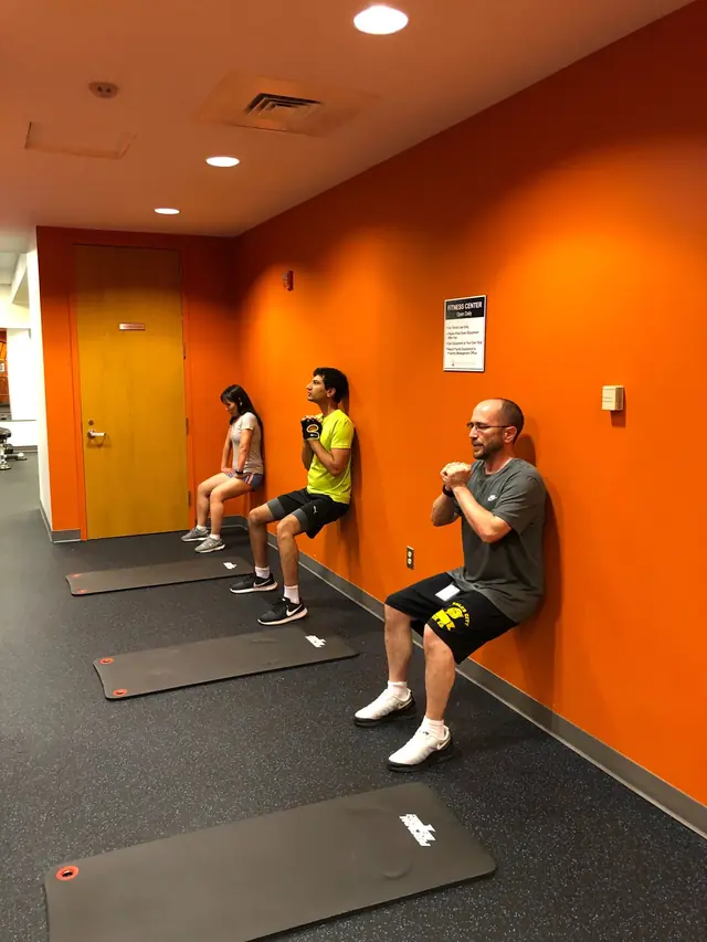 Employees doing wall sits in an office fitness center